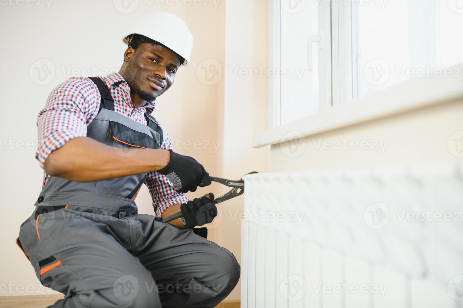 Man in workwear overalls using tools while installing or repairing heating radiator in room photo