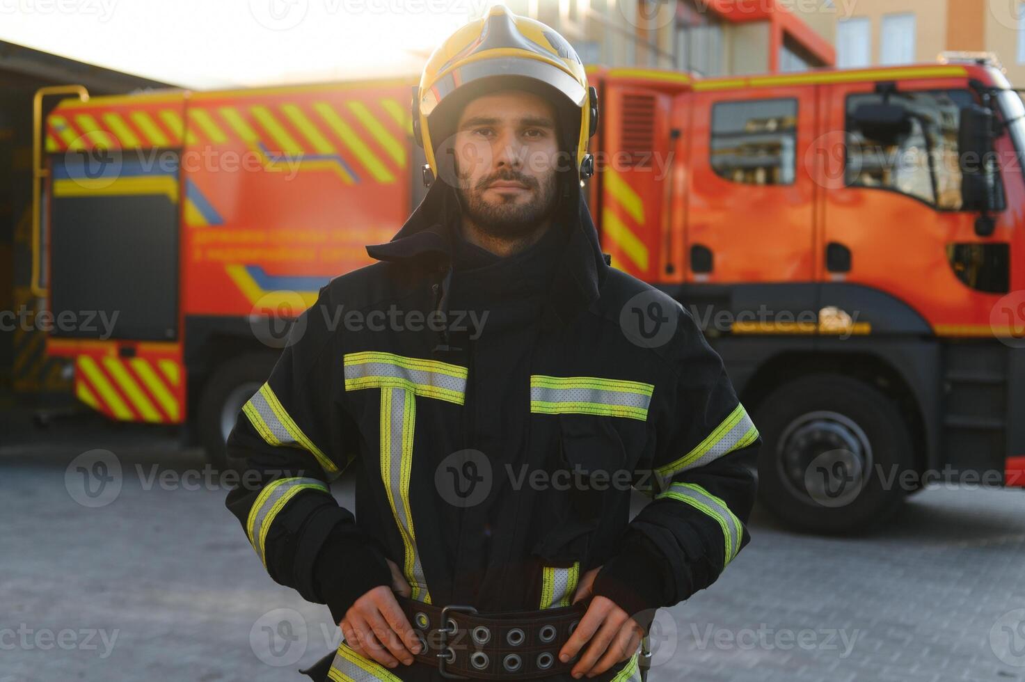 fireman in protective uniform standing near fire engine on station photo