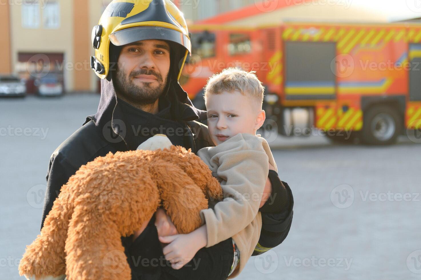 A firefighter take a little child boy to save him. Fire engine car on background photo