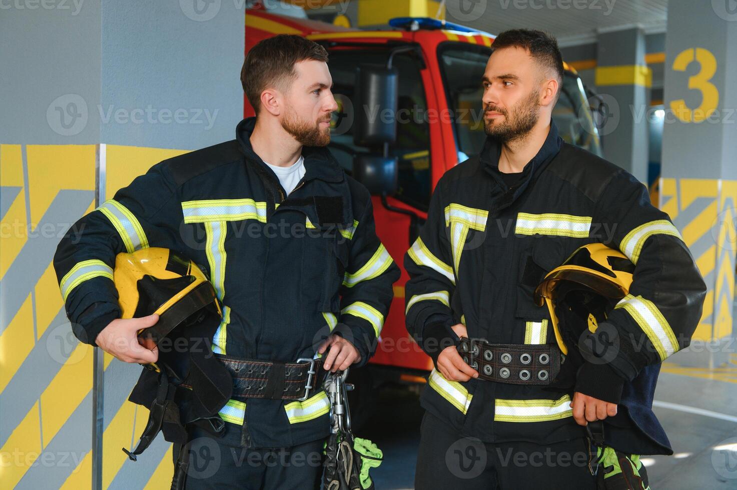 Portrait of two young firemen in uniform standing inside the fire station photo