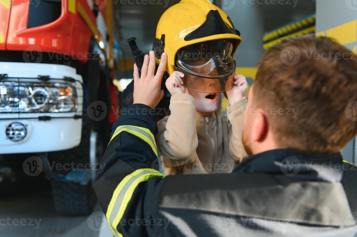 A fireman shows his work to his young son. A boy in a firefighter's helmet photo