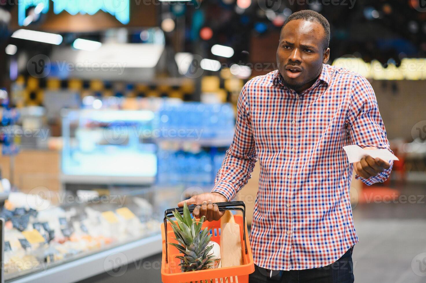 Surprised African-American man looks at receipt total in sales check holding paper bag photo