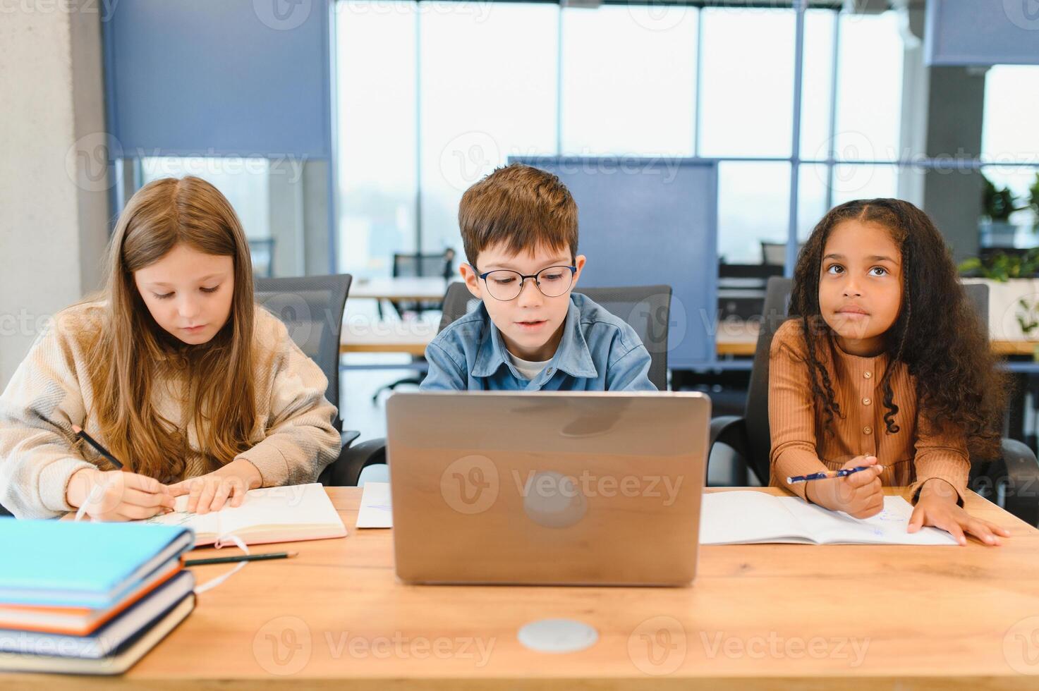 Portrait of smart schoolgirls and schoolboys looking at the laptop in classroom photo