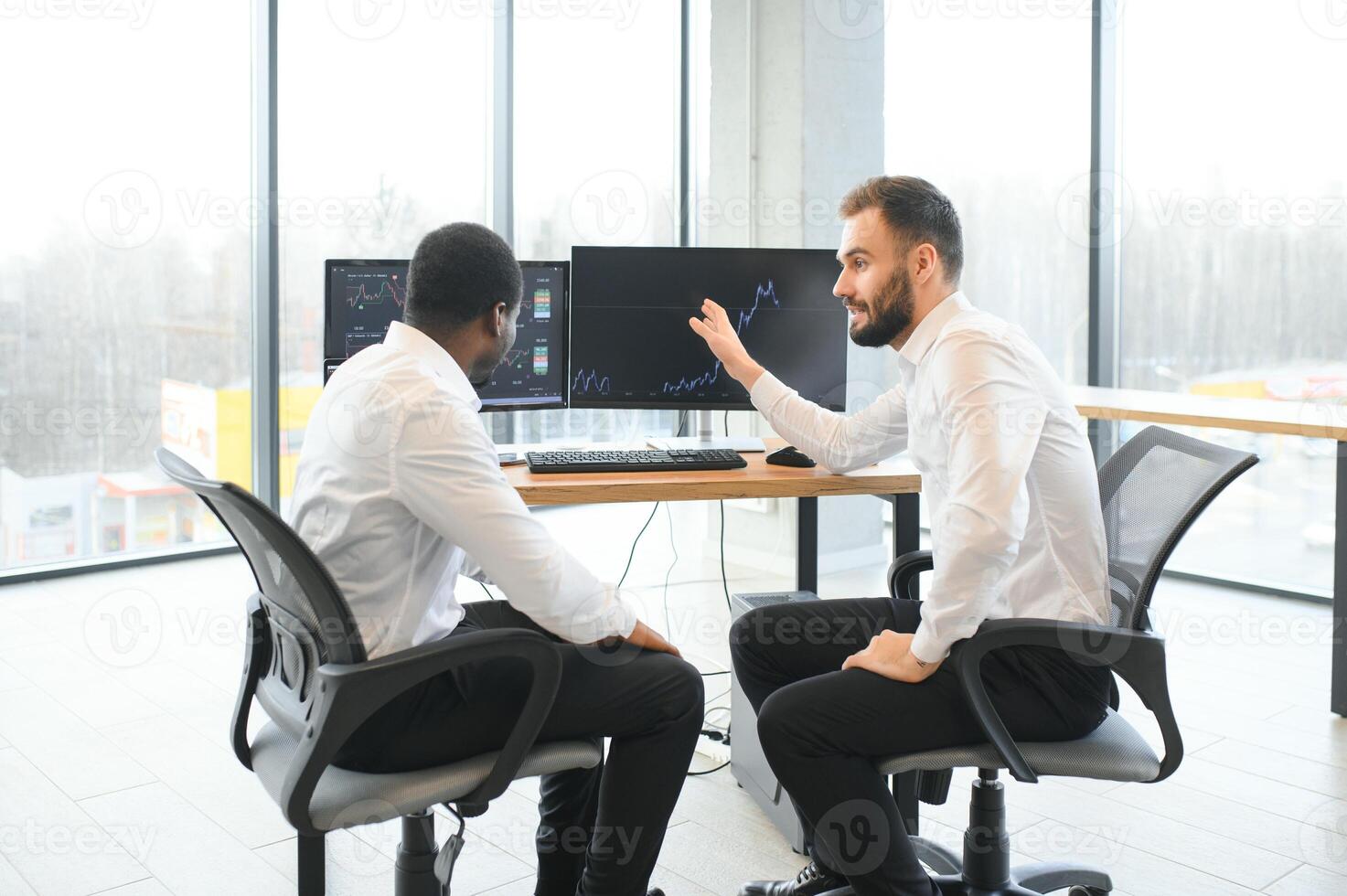 Two successful trader sitting in office, checking cryptocurrency information data on finance market graph, pointing on monitor photo