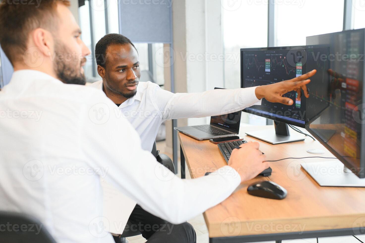 Two successful trader sitting in office, checking cryptocurrency information data on finance market graph, pointing on monitor photo