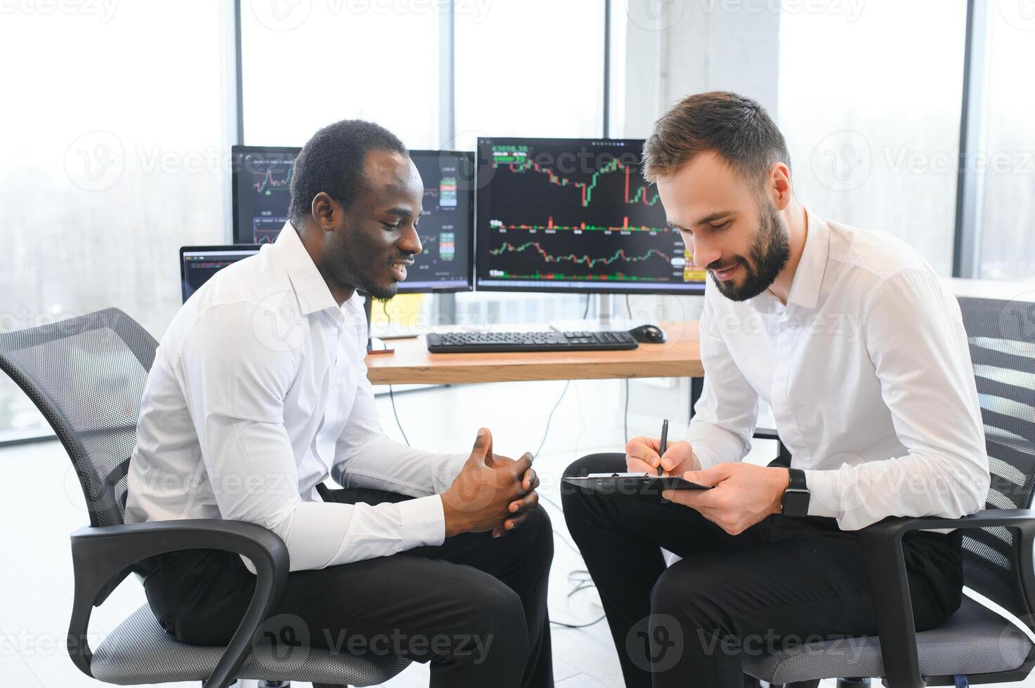Two successful trader sitting in office, checking cryptocurrency information data on finance market graph, pointing on monitor photo