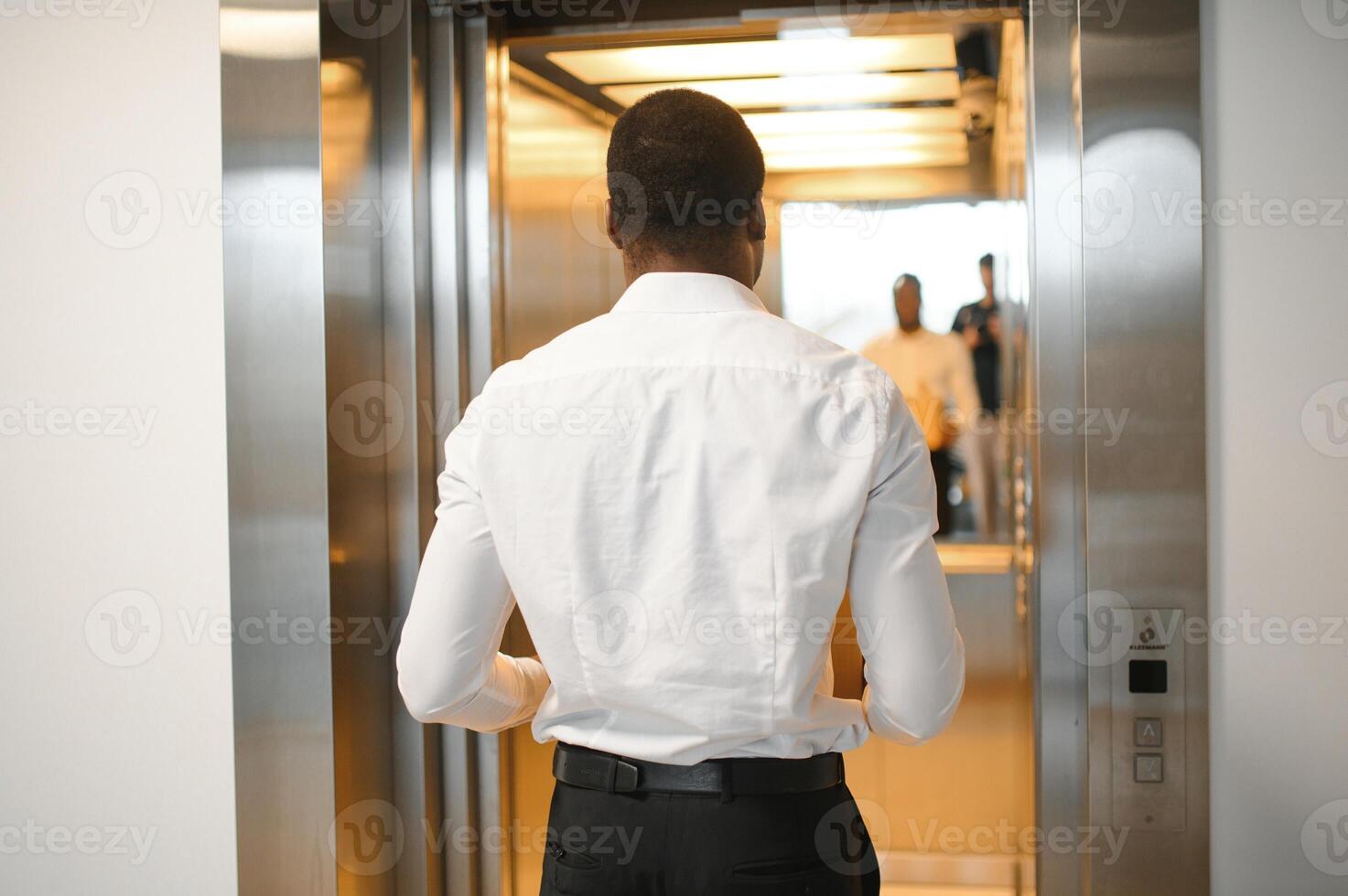 A young african man fired from work is standing in the elevator with a box of things photo
