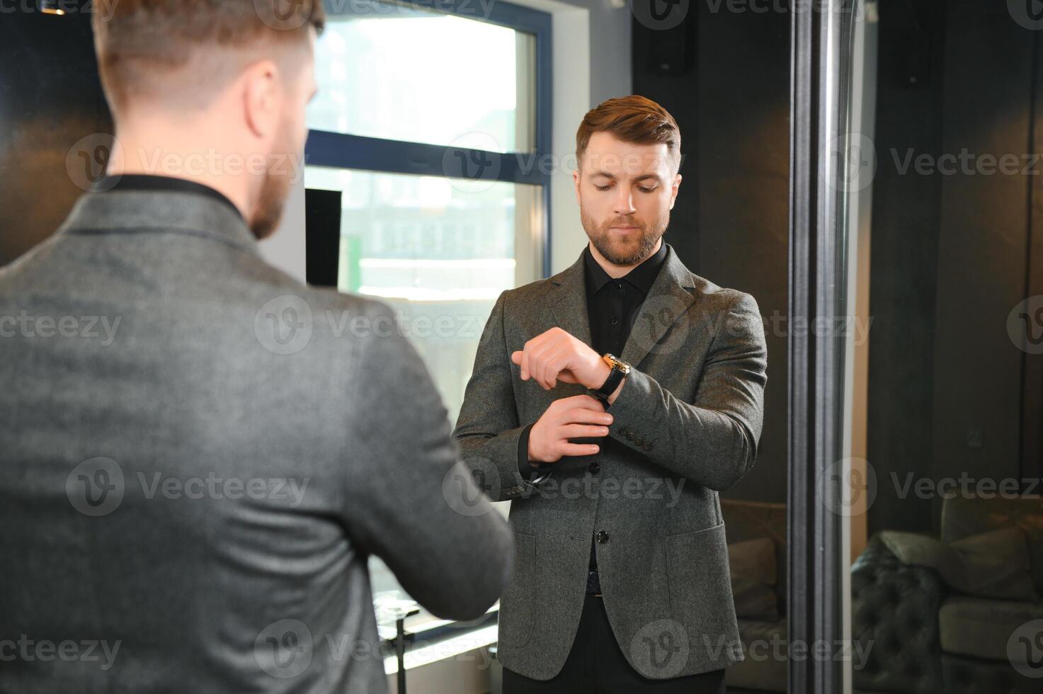 Modern young handsome businessman dressed in classical suit adjusting a tie in front of the mirror while standing in the suit shop photo