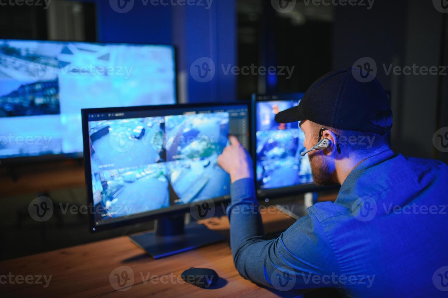 Rear view of security system operator looking at CCTV footage at desk in office photo