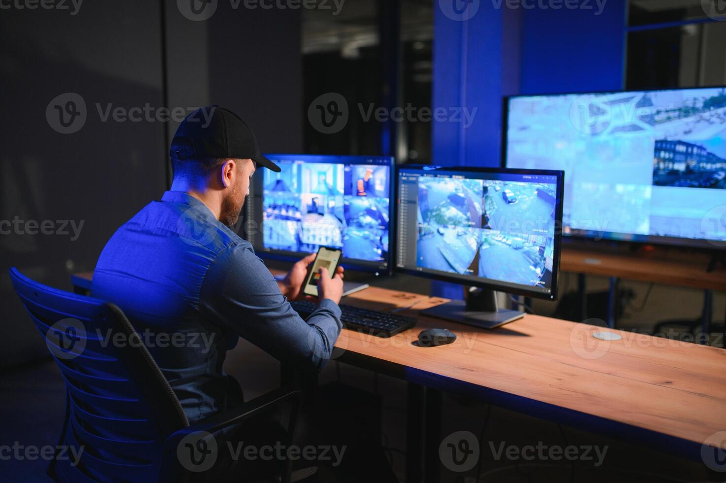 Rear view of security system operator looking at CCTV footage at desk in office photo