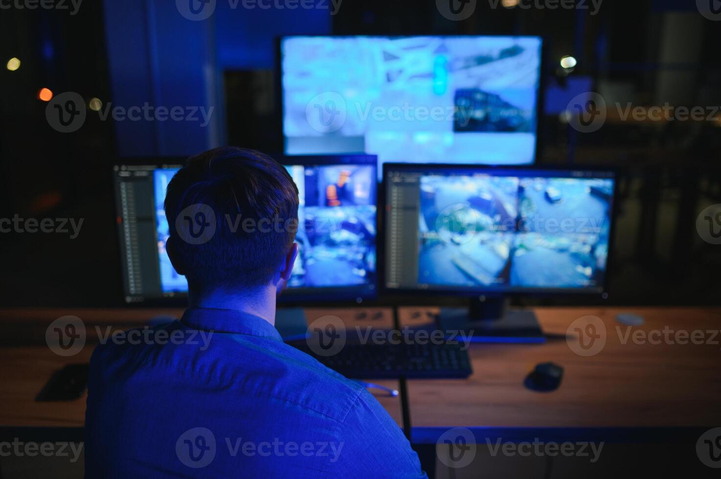 Rear view of security system operator looking at CCTV footage at desk in office photo