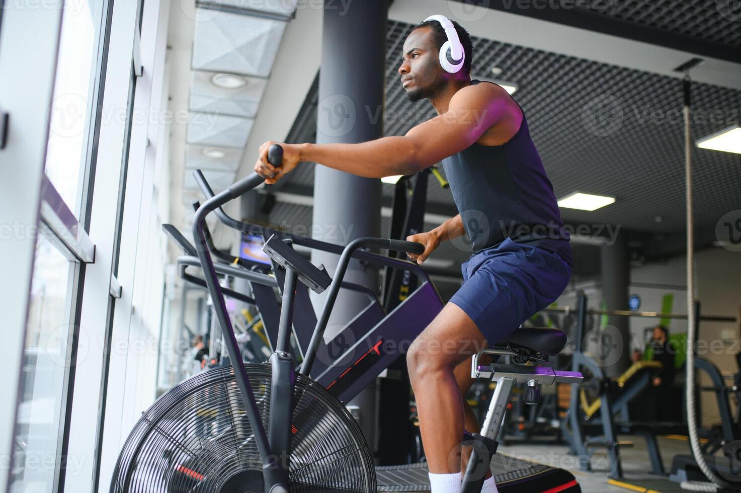 Athletic black man doing cardio workout on exercise bike in gym. Concept of sport and healthy lifestyle photo