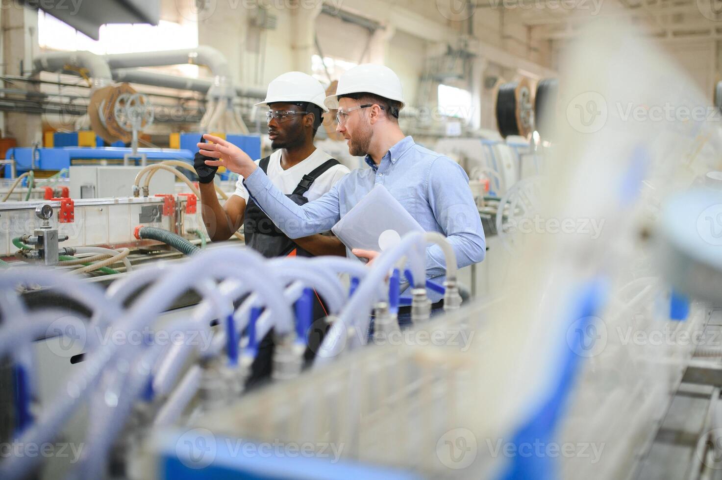 Two Diverse Professional Heavy Industry Engineers Wearing Safety Uniform and Hard Hats Working on Laptop photo