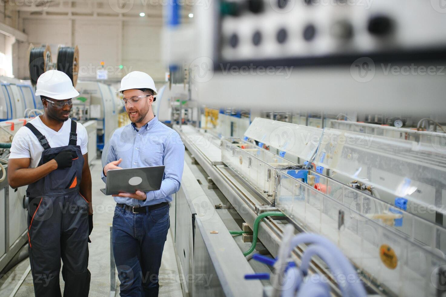 Two Diverse Professional Heavy Industry Engineers Wearing Safety Uniform and Hard Hats Working on Laptop photo