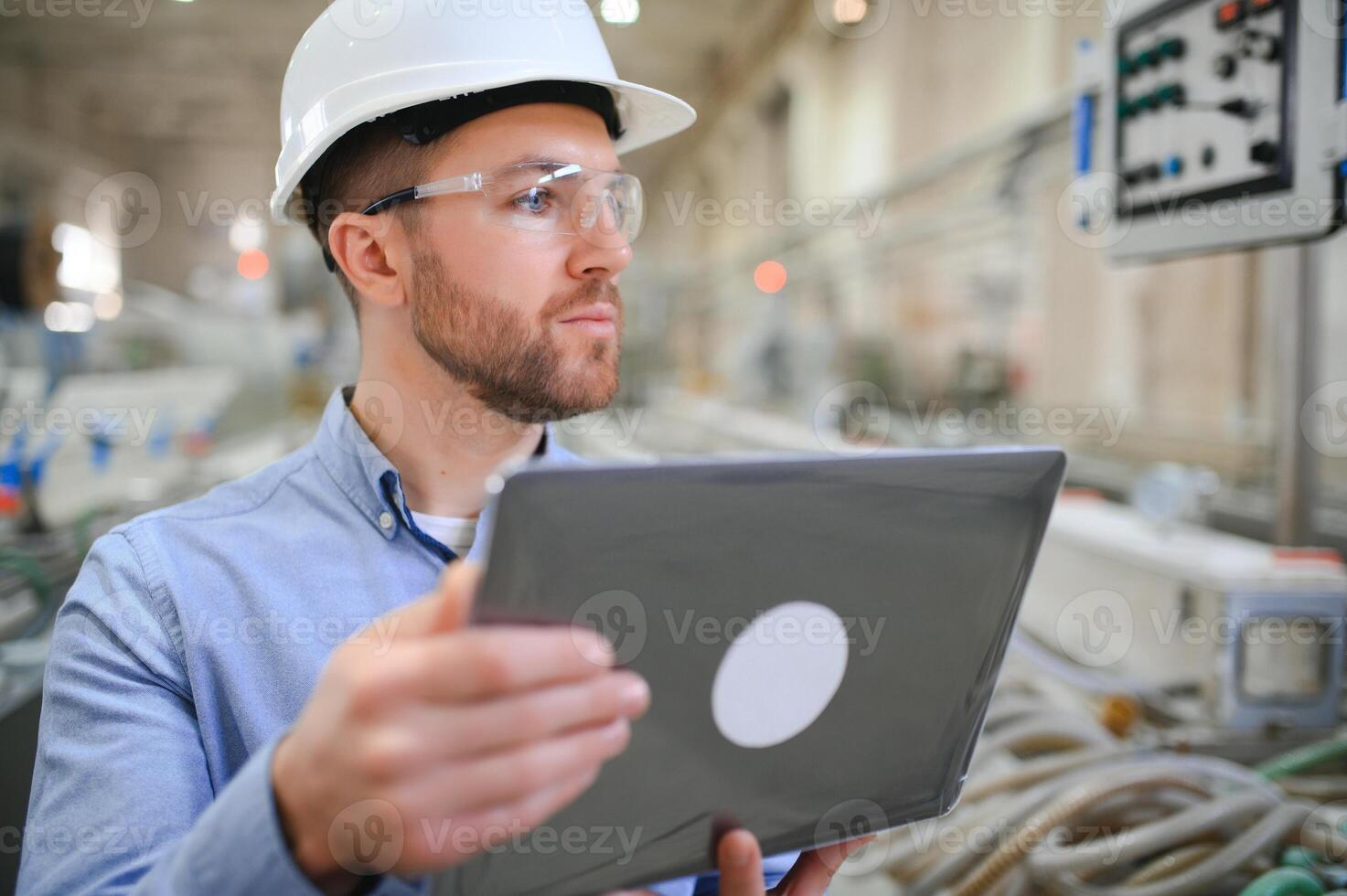 Engineer in hardhat is using a laptop in a heavy industry factory photo