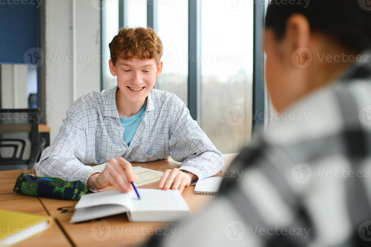 students sit at shared desk making notes studying together at university photo