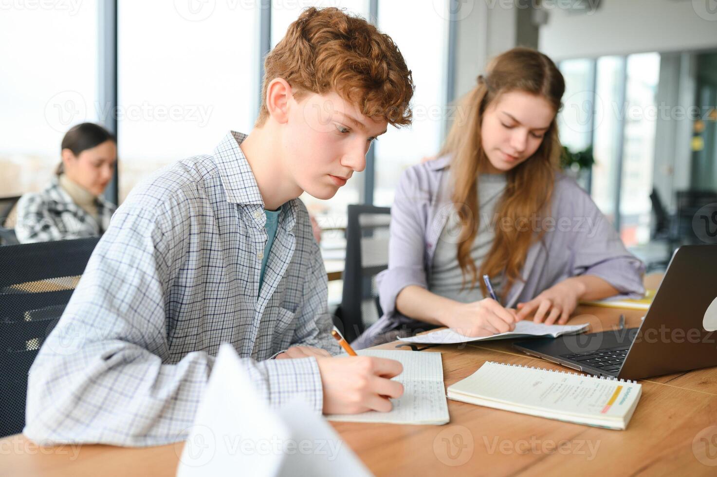 students sit at shared desk making notes studying together at university photo