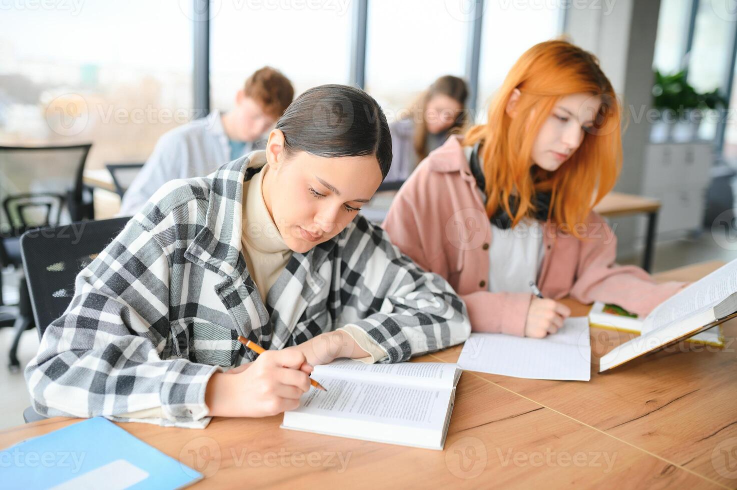 students sit at shared desk making notes studying together at university photo