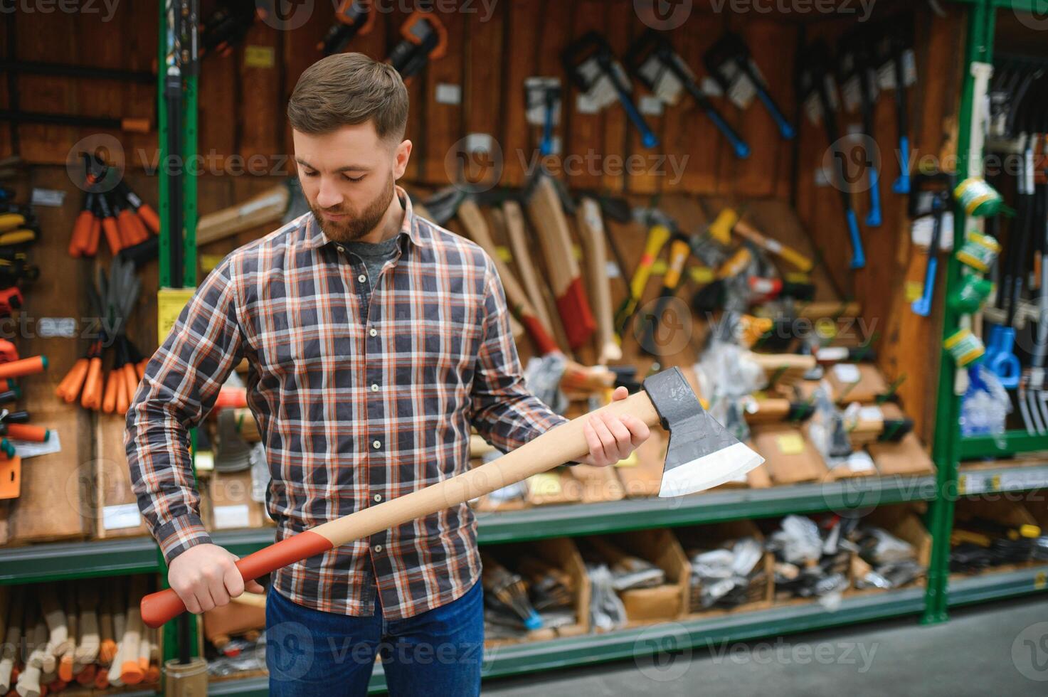 A young man chooses axe in the hardware store photo