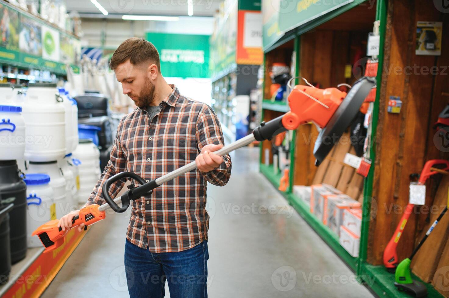 a young man in a gardening equipment store chooses an electric trimmer for mowing lawn grass photo