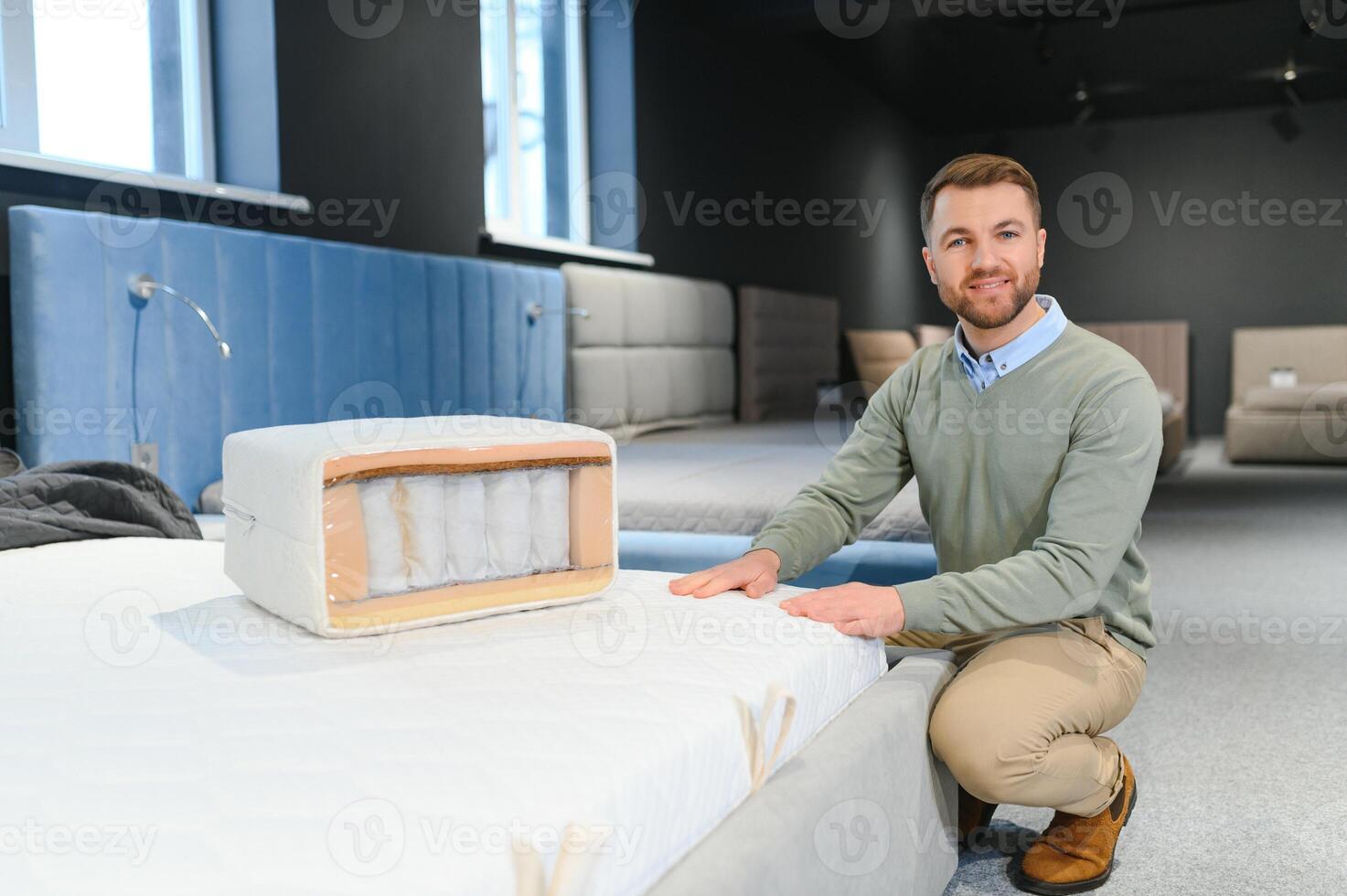 Handsome man examining sample of orthopedic mattress on sale photo