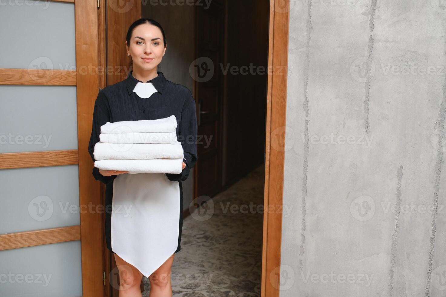 The maid is standing in the corridor of the hotel and holding clean towels photo
