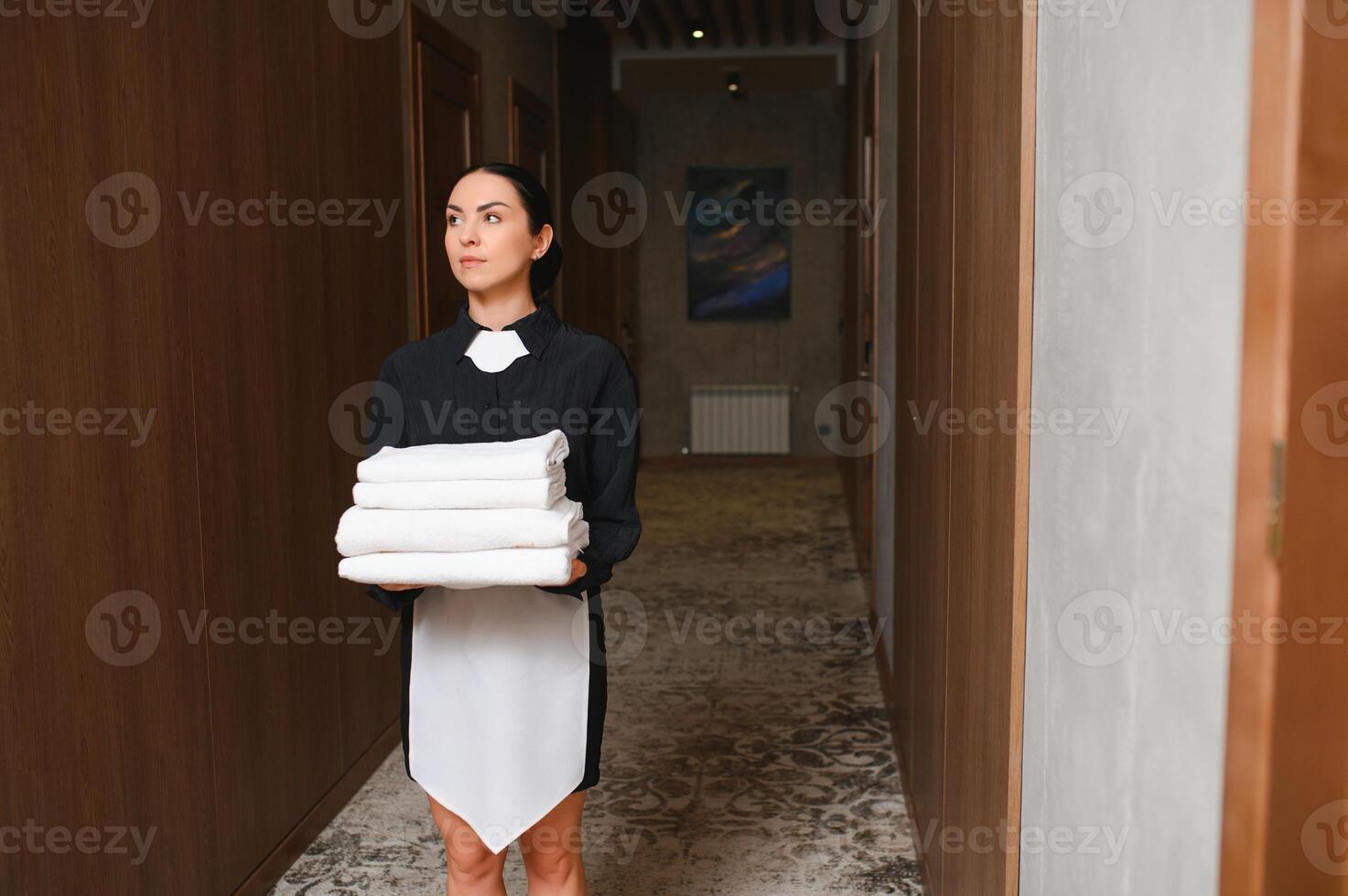 The maid is standing in the corridor of the hotel and holding clean towels photo