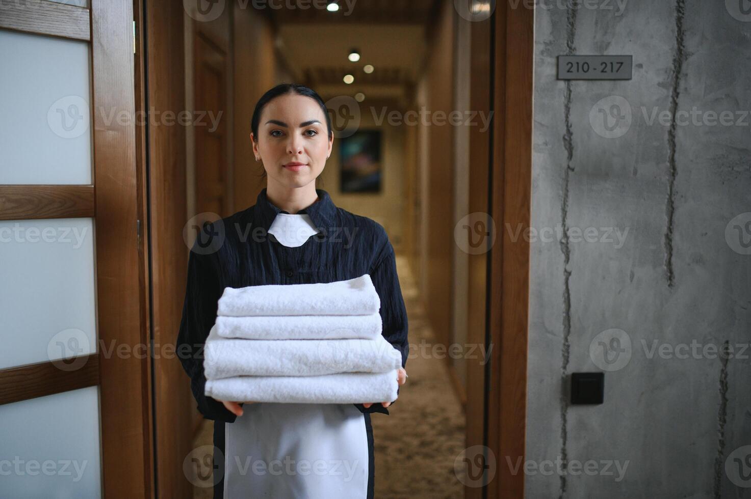 The maid is standing in the corridor of the hotel and holding clean towels photo