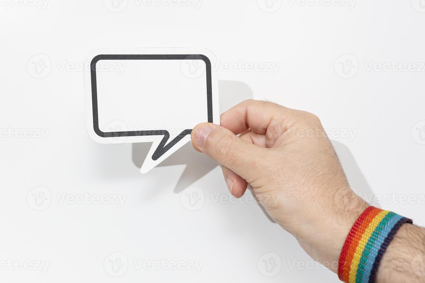 Hand wearing pride flag bracelet holding blank speech bubble on white background. Template Mockup photo