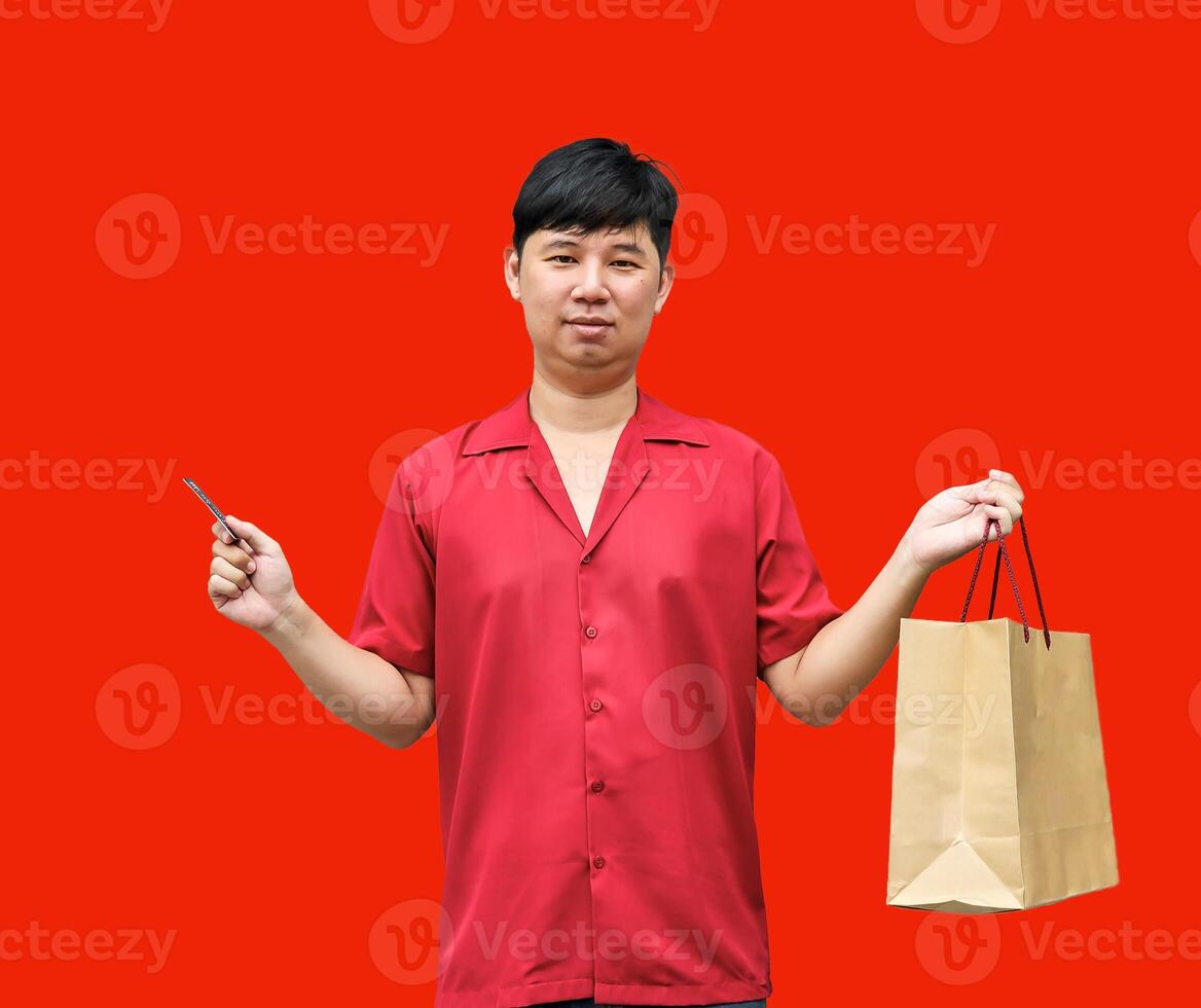 joyful Asian man carrying shopping bags and a credit card. on red background. Chinese New Year theme photo