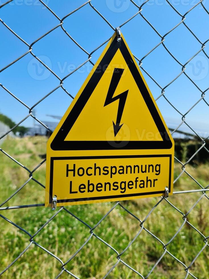 A warning sign with the German inscription for high voltage danger to life on the fence of a solar park photo