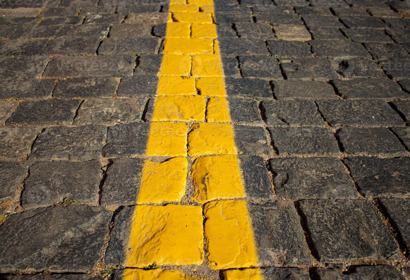 The texture of dark paving stones. The yellow stripe. An old stone sidewalk. The texture of the paving stones. The background is made of cobblestones, the road is made of cobblestones. photo