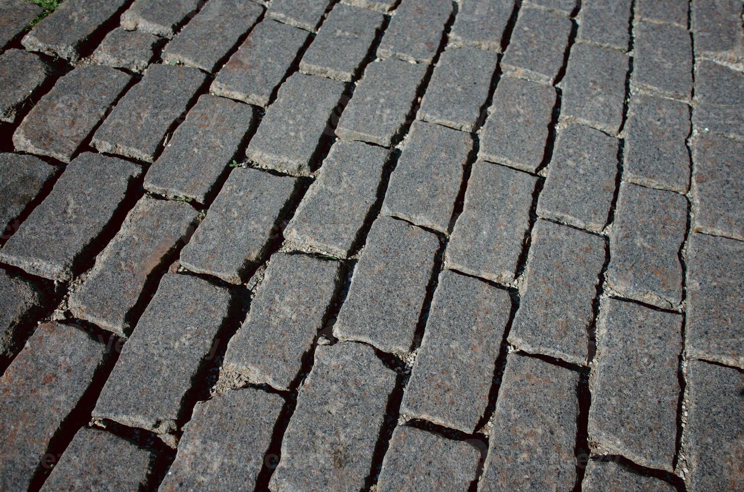 The texture of dark paving stones. Top view of the cobblestone pavement. An old stone sidewalk. The texture of the paving stones. The background is made of cobblestones, the road is made of cobbleston photo