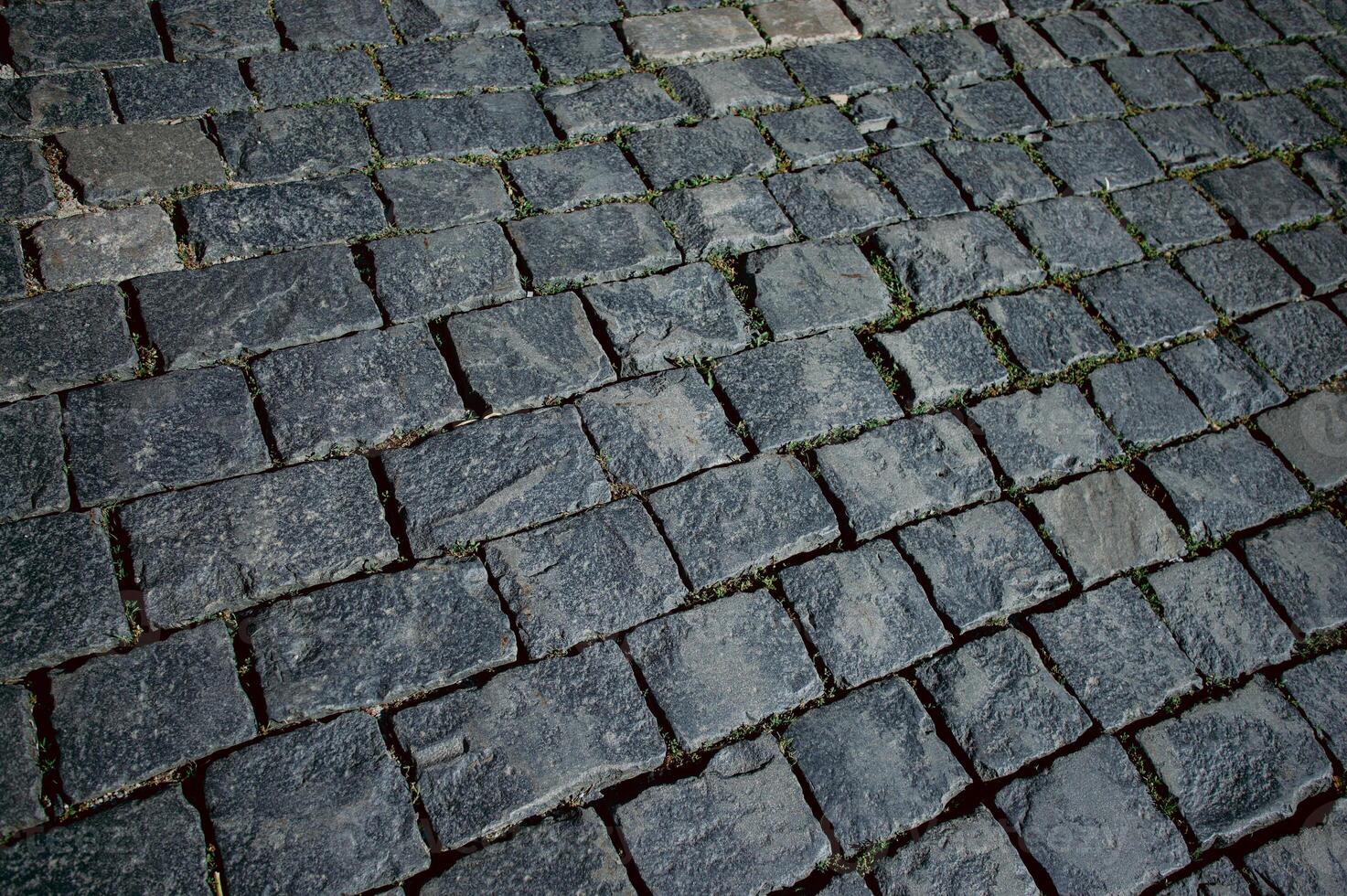 The texture of dark paving stones. Top view of the cobblestone pavement. An old stone sidewalk. The texture of the paving stones. The background is made of cobblestones, the road is made of cobbleston photo