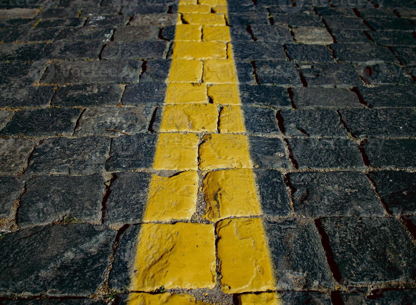 The texture of dark paving stones. The yellow stripe. An old stone sidewalk. The texture of the paving stones. The background is made of cobblestones, the road is made of cobblestones. photo