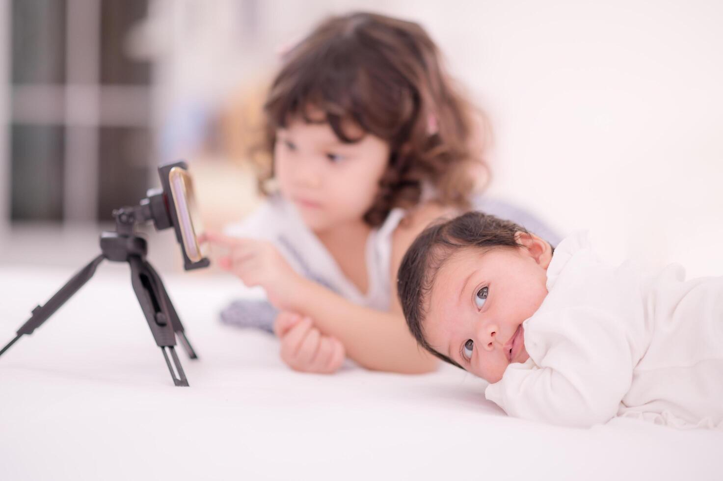 A cute Asian girl is looking at her mobile phone set to take a picture of herself and her newly born sister photo