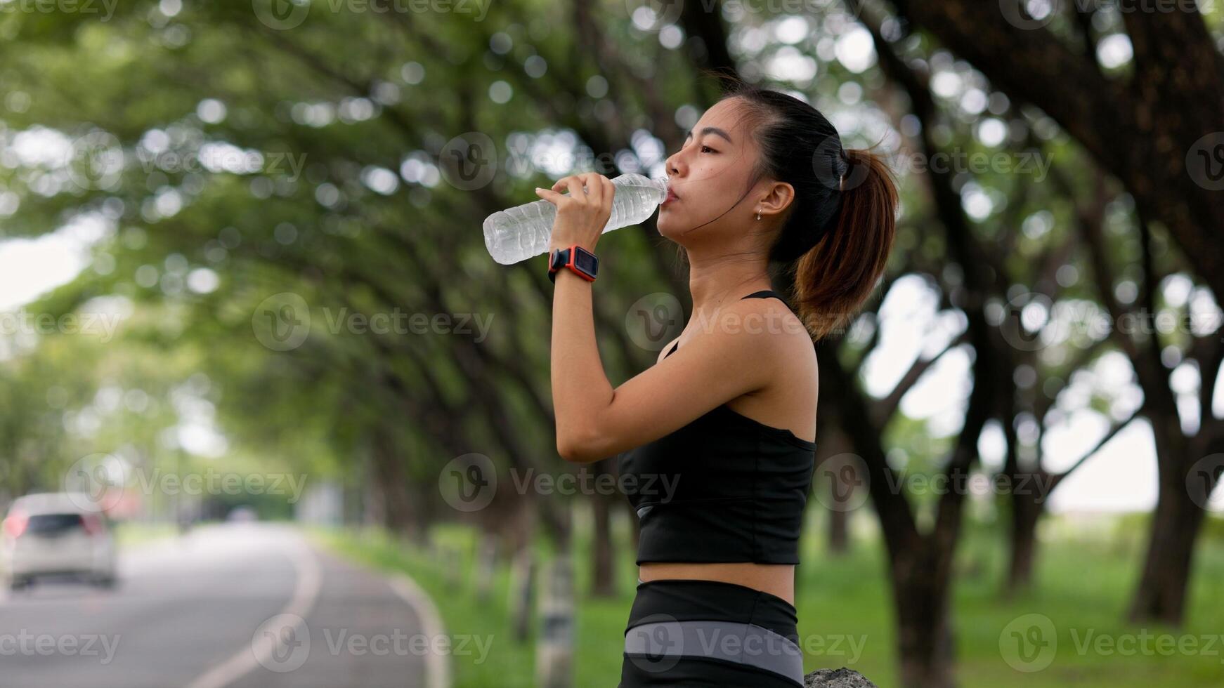 A woman is drinking water while walking on a road photo