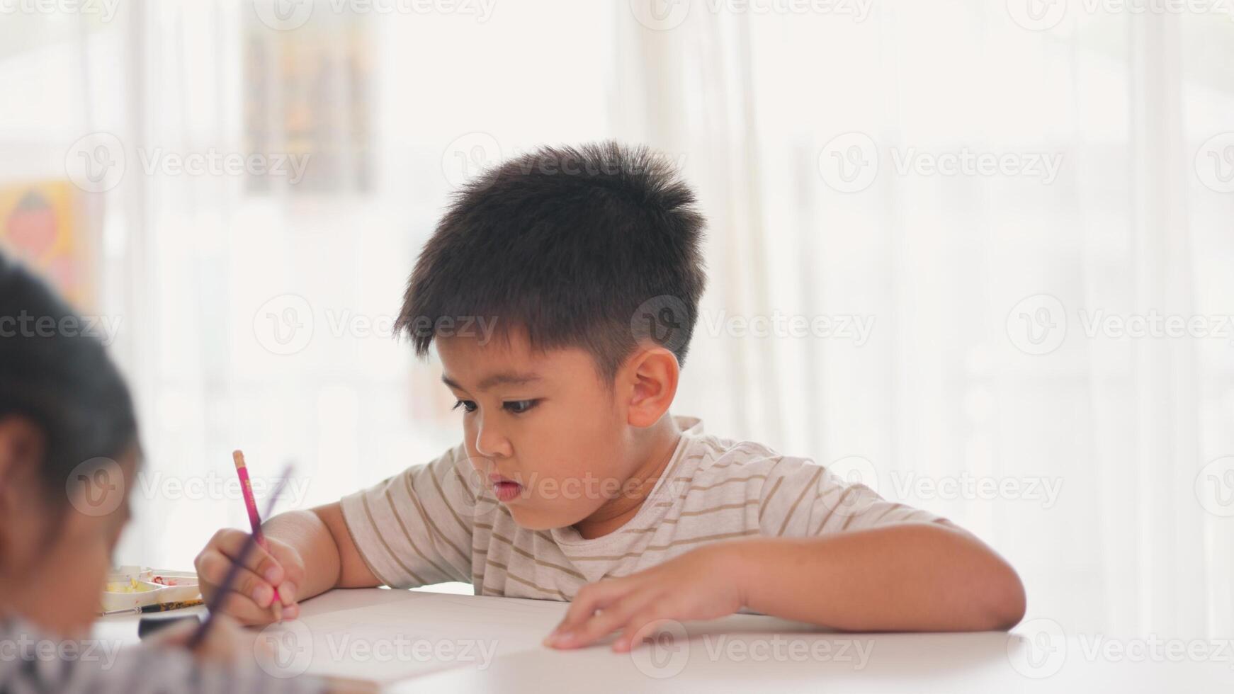 A boy is writing with a pink pencil on a piece of paper photo