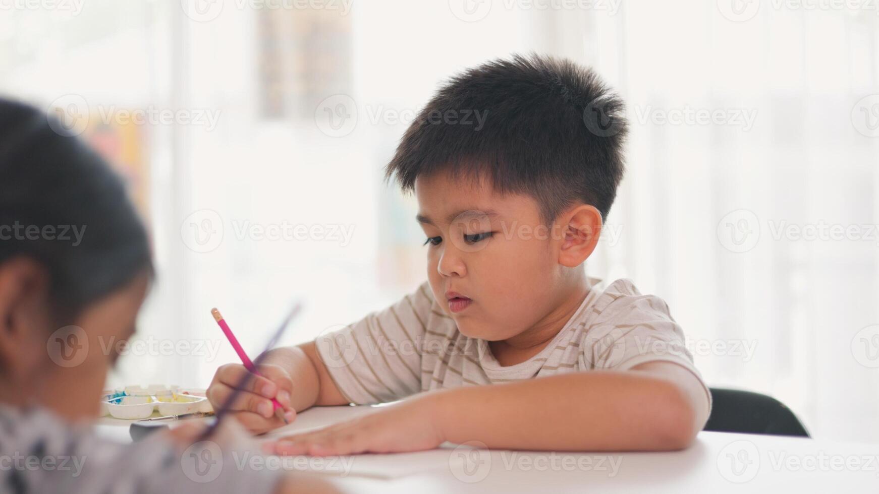 A boy is writing with a pink pencil on a piece of paper photo