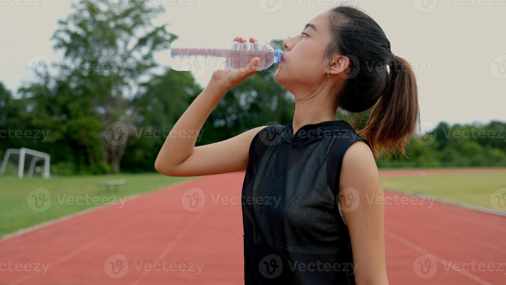 A woman is drinking water while standing on a track photo