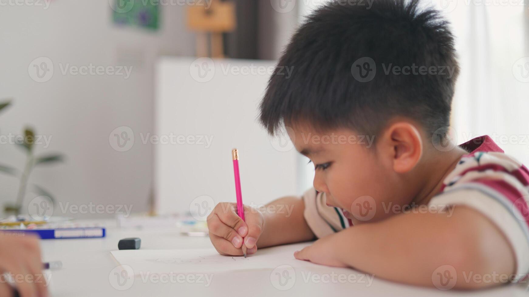 A boy is writing with a pink pencil on a piece of paper photo