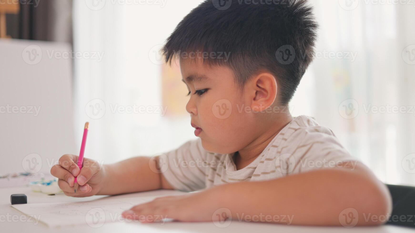 A boy is writing with a pink pencil on a piece of paper photo