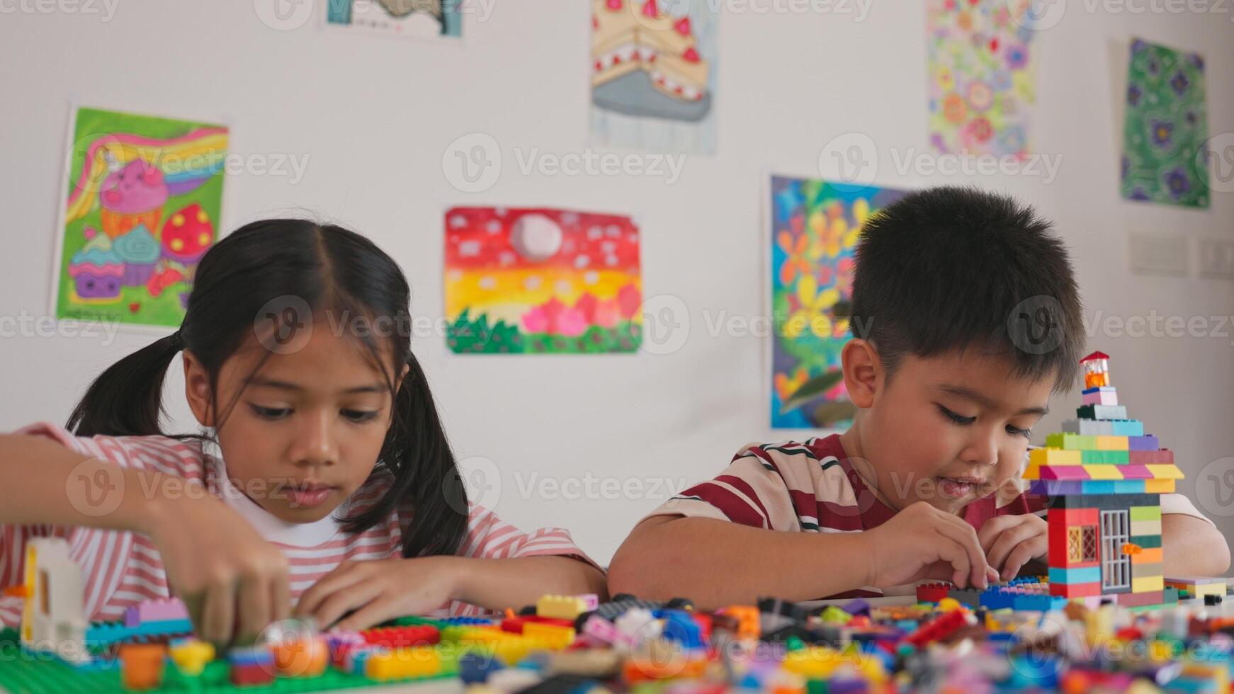 Two children are playing with legos in a room with colorful pictures on the wall photo