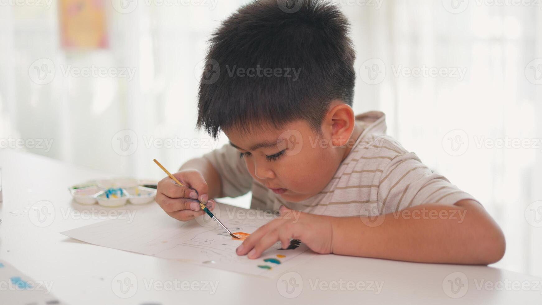 A young boy is painting a picture on a white table photo