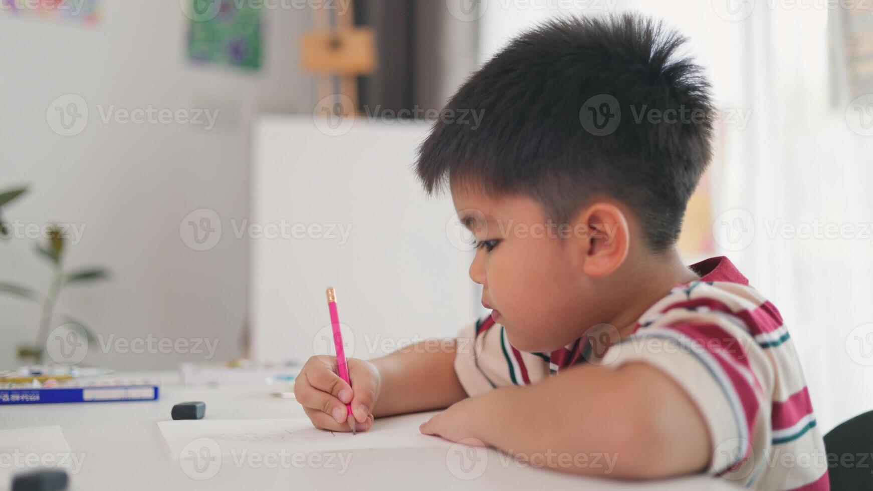 A boy is writing with a pink pencil on a piece of paper photo