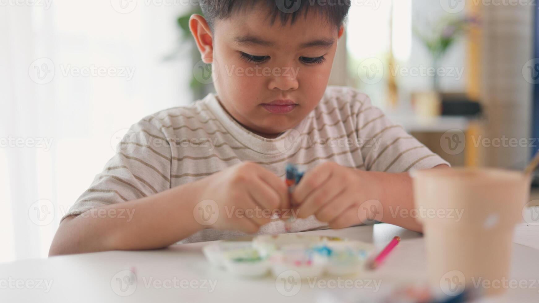 A young boy is painting a picture on a white table photo