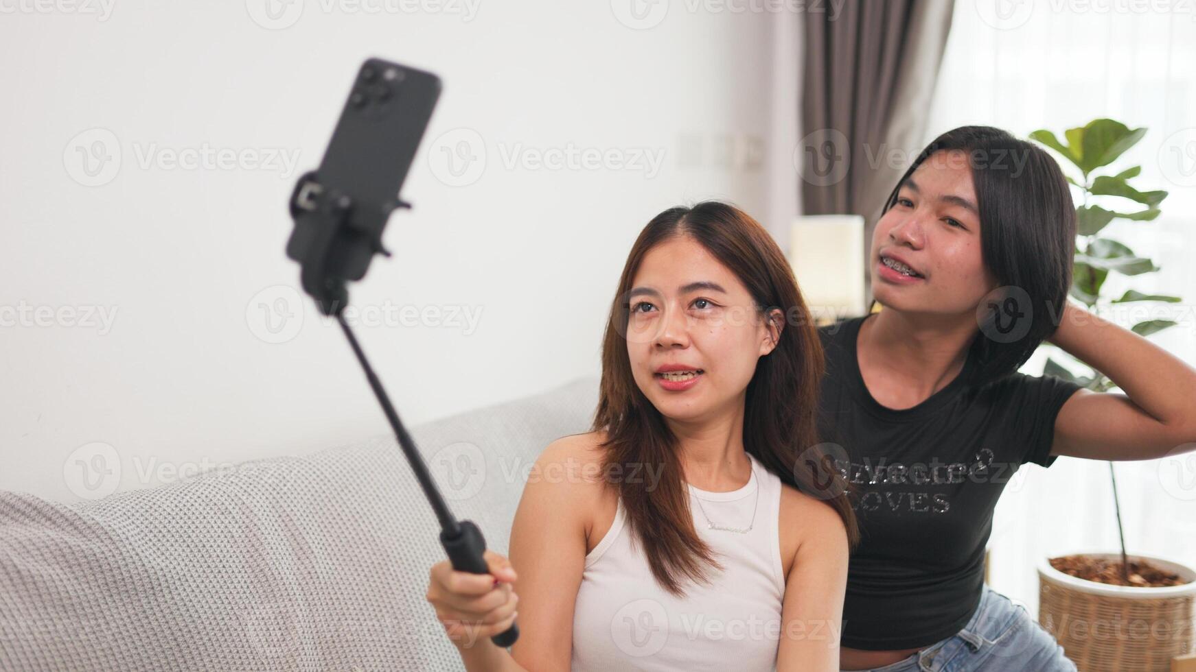 Girl and LGBTQ friend are sitting on a cozy couch, taking a selfie with a cell phone, capturing their happy moment together. photo