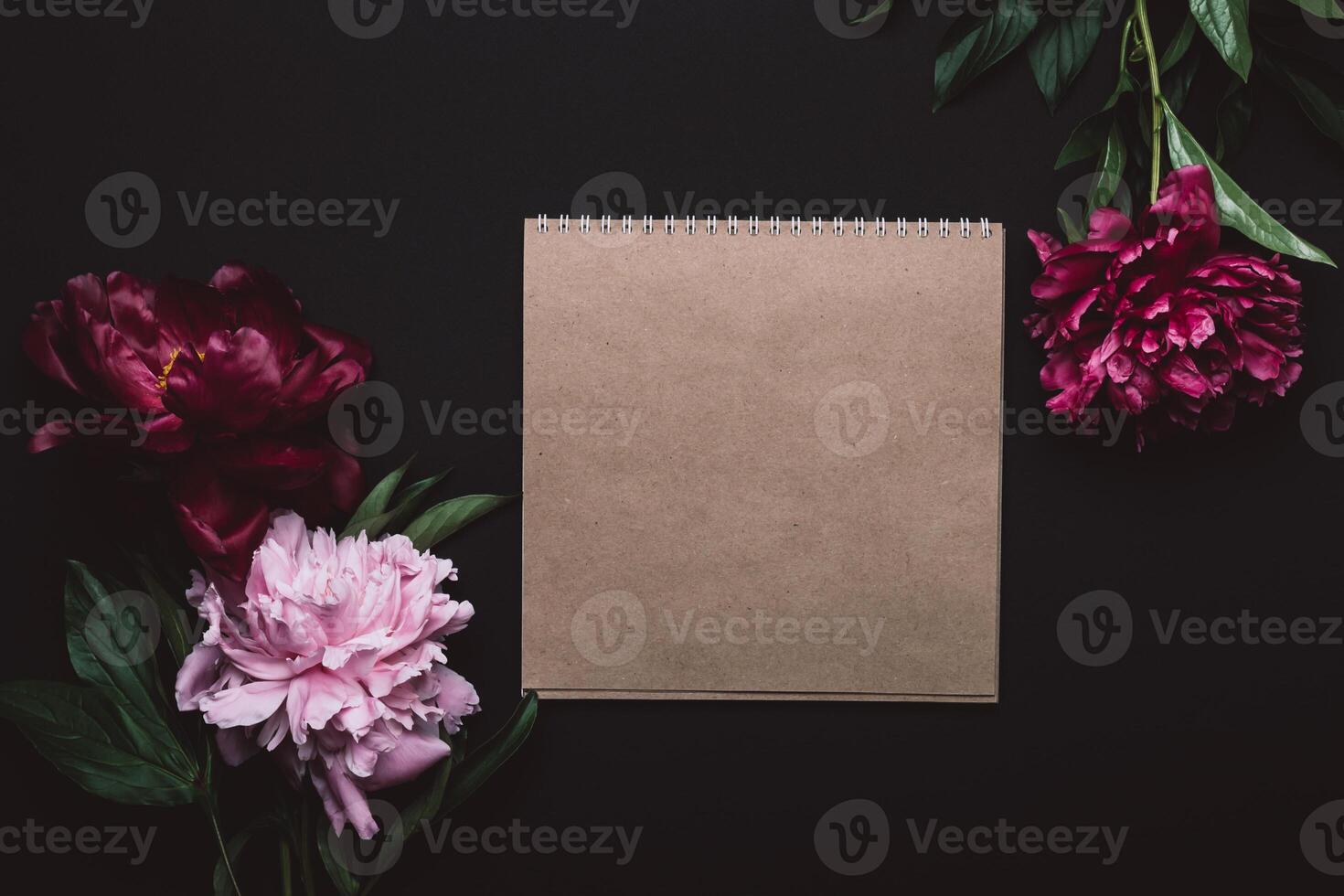 Beautiful peonies in dark colors and notebook. Black Floral background. Soft focus, copy space photo
