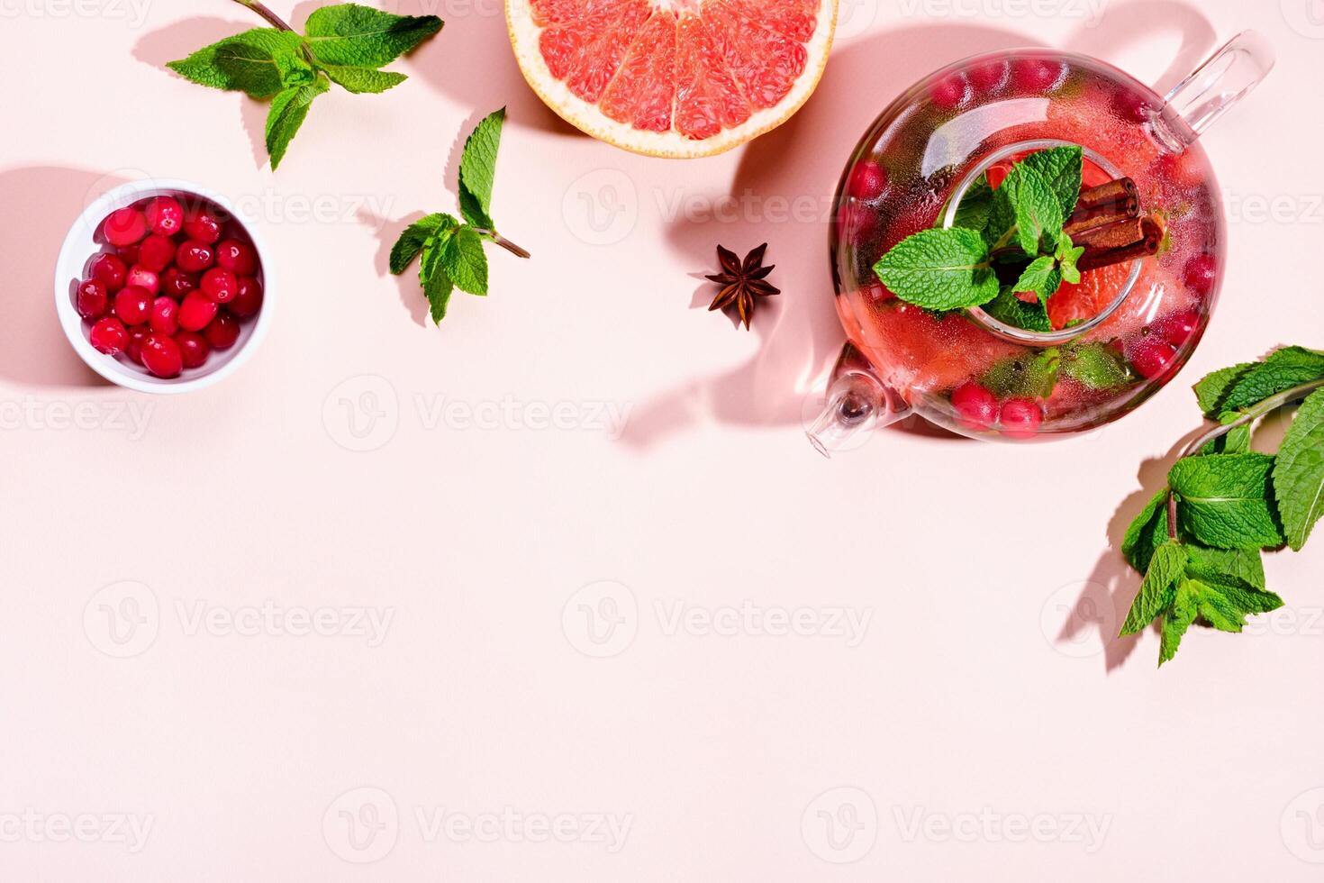 Immunity boosting drink. Mint Tea with cranberries, grapefruit and spices in glass teapot on pink table, trendy shadows photo
