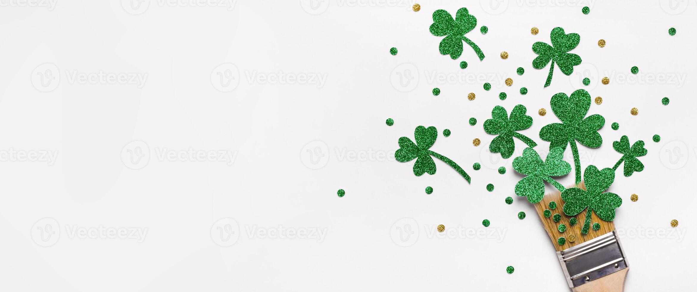 Creative St. Patricks Day concept made with paint brush and green glitter shamrocks and confetti. Banner format photo